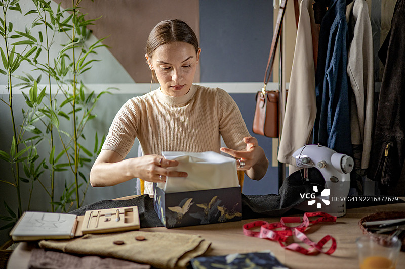 在她的小型精品店里，一位年轻女性认真地将一件定制的服装折叠并装入一个运输箱，准备寄给她的小型企业的顾客。图片素材