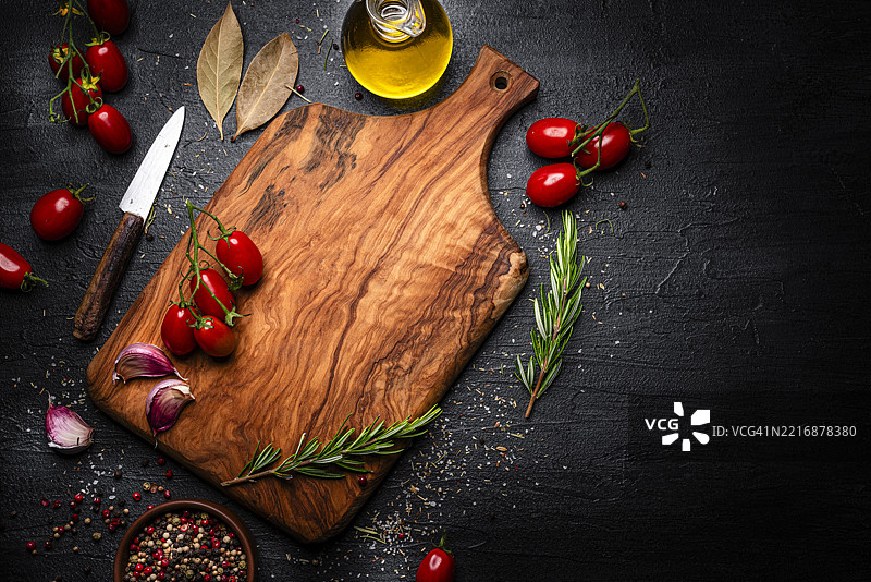 黑色桌子上的蔬菜、香草和调味品。健康新鲜的食材围绕着一个空的切菜板。留白空间。图片素材