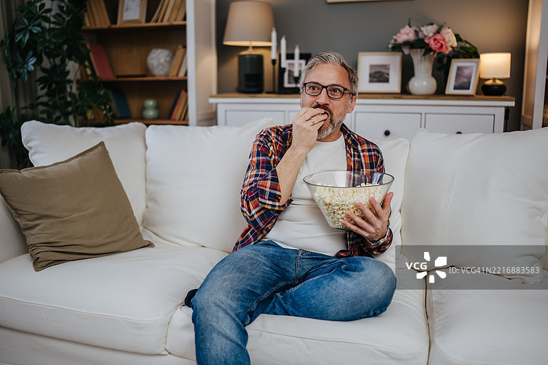 成熟男人坐在沙发上看电视，吃着爆米花图片素材