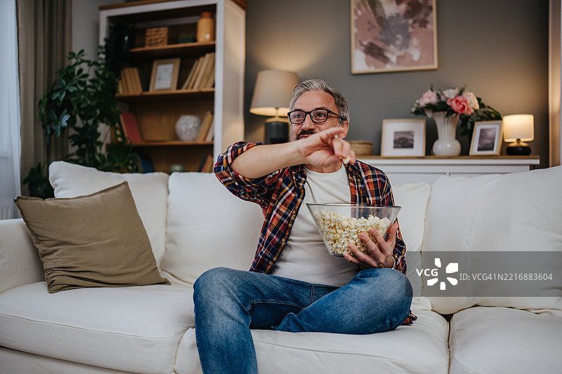 成熟男人坐在沙发上看电视，吃着爆米花图片素材