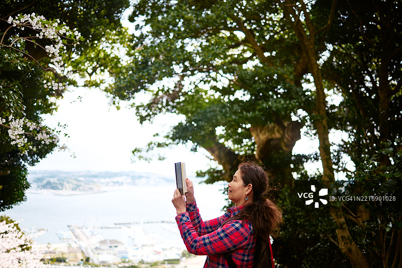 一位年长女性在宁静的自然环境中放松，阅读一本书，周围环绕着生机勃勃的绿意。图片素材
