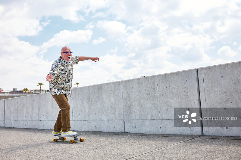 一位快乐的老年男子骑着滑板，脸上挂着灿烂的笑容，显然在享受着他在街道上滑行的时刻。图片素材