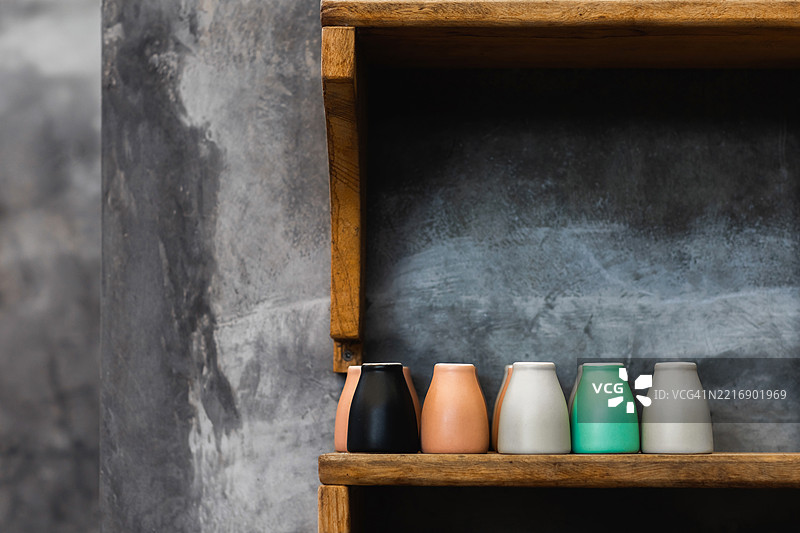 不同颜色的咖啡杯摆放在咖啡馆的木架上。背景是灰色混凝土墙。时尚的室内设计，潮流咖啡馆。留有空白以便添加文字。图片素材