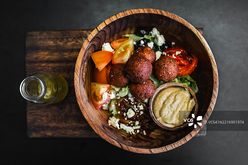 木碗里装着法拉费球、鹰嘴豆泥和新鲜沙拉。旁边有一瓶橄榄油。黑色背景，俯视图。传统以色列美食。素食主义概念。图片素材