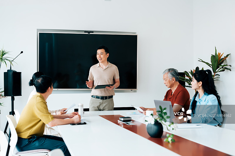 成熟的亚洲商人在现代会议室使用数字平板电脑并展示计划。年轻的亚洲商人有手指残疾。图片素材