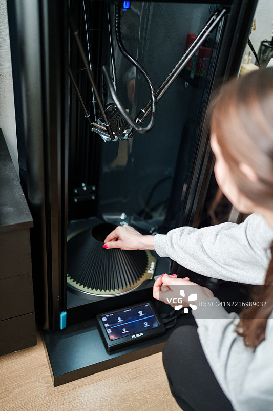 女性在家中工作室操作3D打印机控制面板图片素材