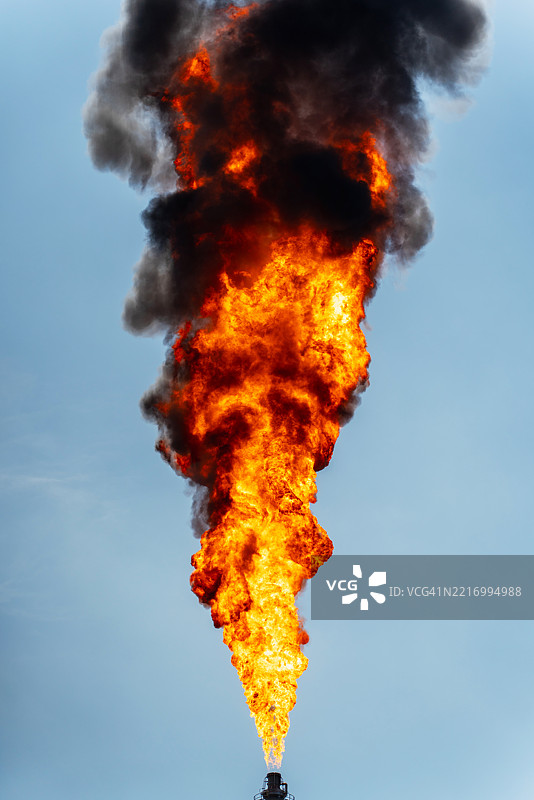 一座巨大的工业厂房被高耸的机械和管道环绕，火焰从燃烧塔喷射而出，照亮了天空。图片素材