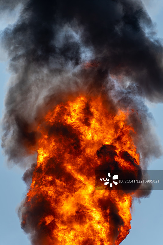 一座巨大的工业厂房被高耸的机械和管道环绕，火焰从燃烧塔喷射而出，照亮了天空。图片素材
