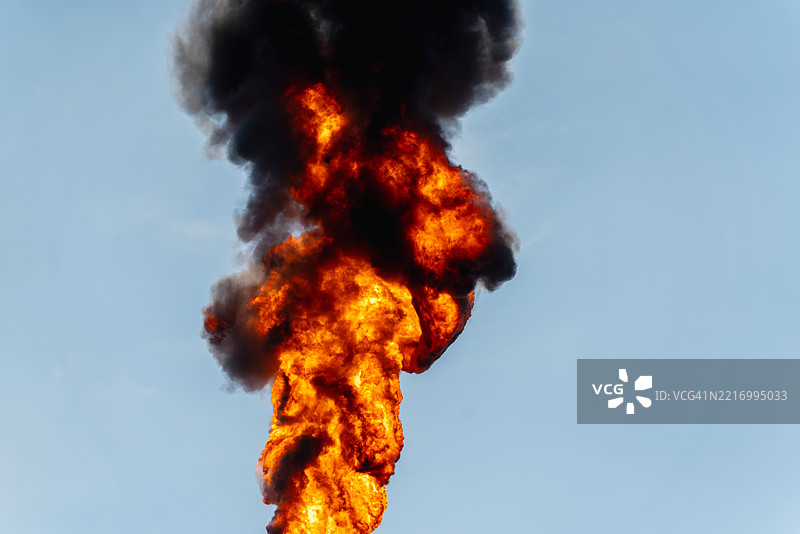 一个巨大的工业厂房被高耸的机械和管道环绕，火焰从燃烧塔喷射而出，照亮了天空。图片素材