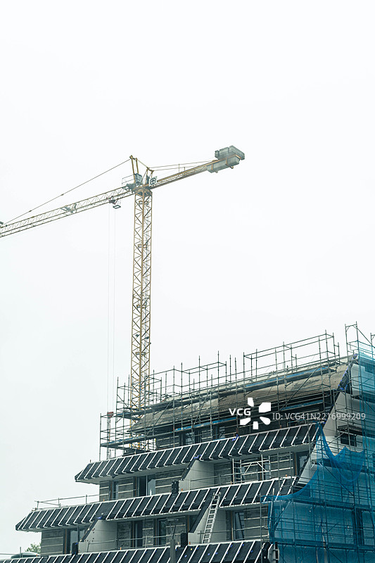 在阴云密布的天空下，建筑起重机正在建设现代公寓综合体图片素材