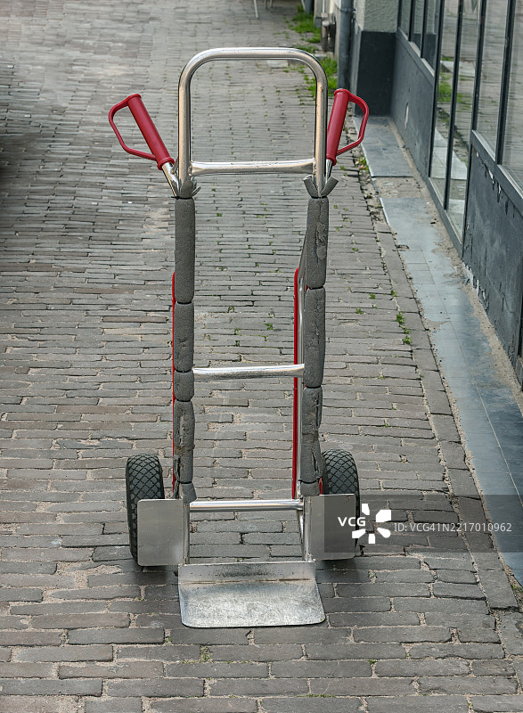 带有红色塑料手柄的金属手推车停在街道上图片素材