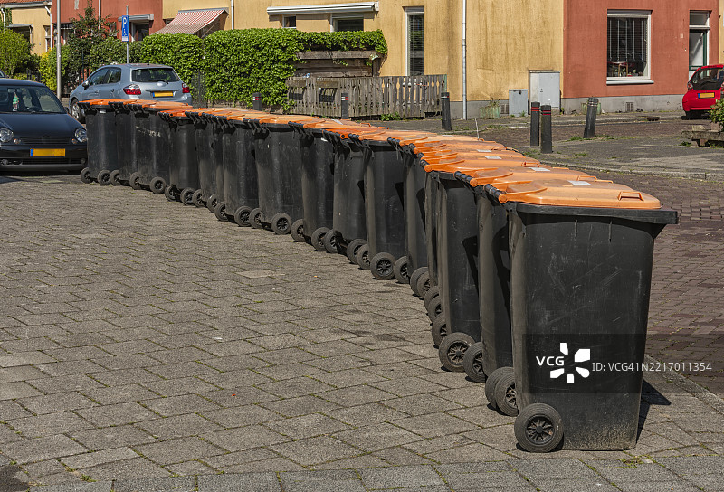 一排黑色垃圾容器，橙色盖子，放置在街道上。图片素材