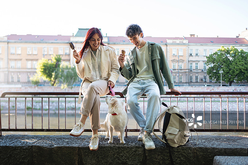 两个朋友在城市公园里与一只快乐的狗享受户外时光图片素材