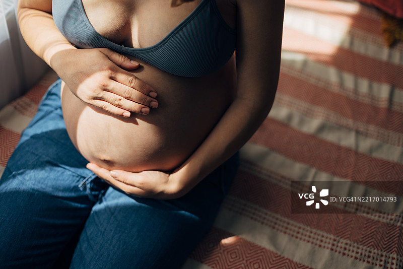 孕妇坐在床上，轻抚着她的肚子图片素材