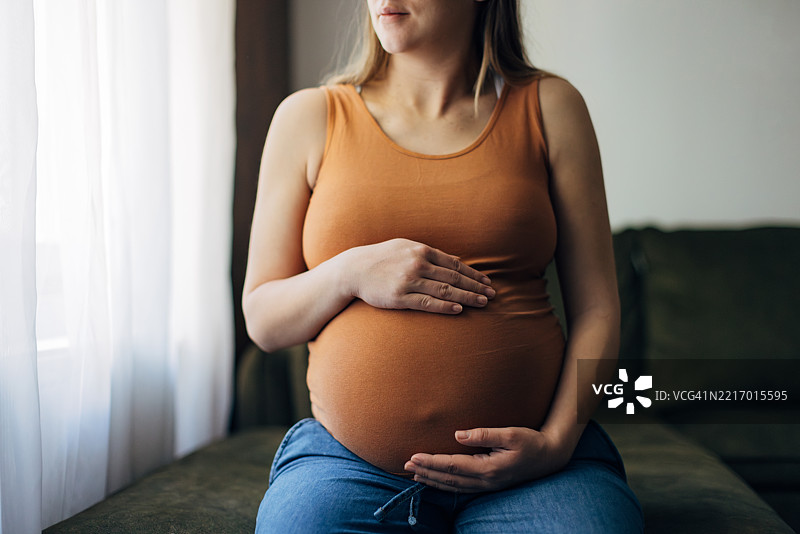孕妇坐在床上，轻抚着自己的肚子图片素材