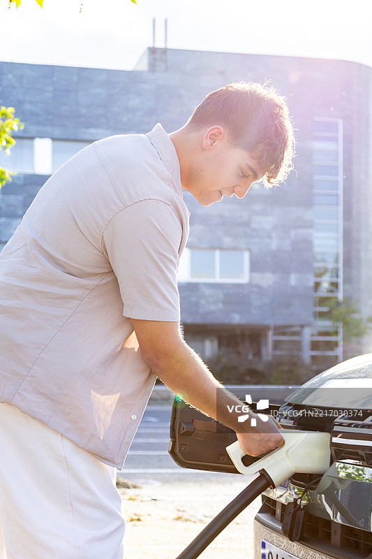 年轻男子在公共充电站为电动车充电图片素材