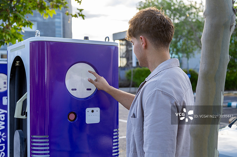 年轻男子正在使用电动车充电站图片素材