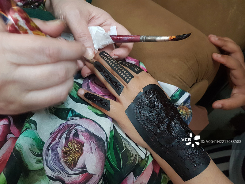 母亲在女儿的手上涂抹海娜纹身或图案。图片素材