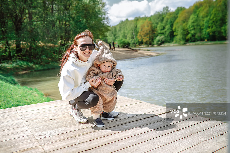 中年妈妈戴着墨镜，和她穿着毛绒连体衣的小女孩一起在码头享受阳光明媚的春日。图片素材