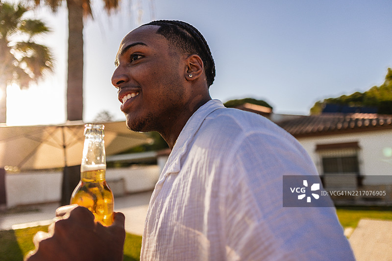 年轻男子在泳池派对上微笑着拿着一瓶啤酒图片素材