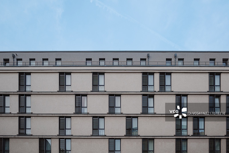 公寓楼具有对称的线条和重复的垂直窗户面板，配有狭窄的百叶窗。图片素材