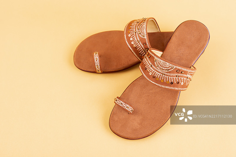 一双棕色凉鞋放在黄色背景上。女性鞋子极简风格。图片素材