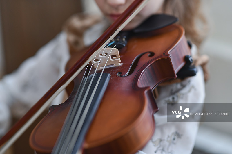 年轻女孩的手优雅地控制着琴弓，专注地拉着小提琴。图片素材