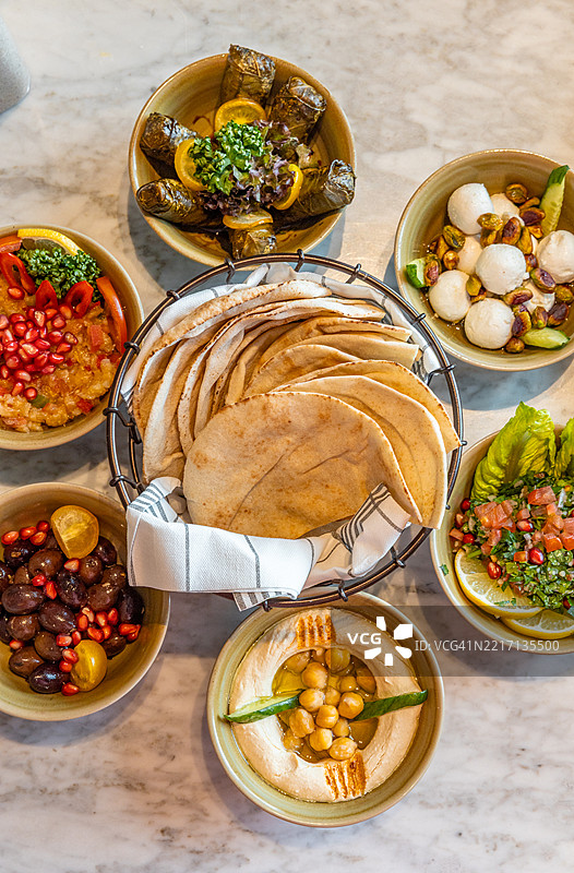阿拉伯小吃拼盘，包括鹰嘴豆泥、茄子酱、酸奶酱和葡萄叶，适合中东美食的午餐桌。图片素材