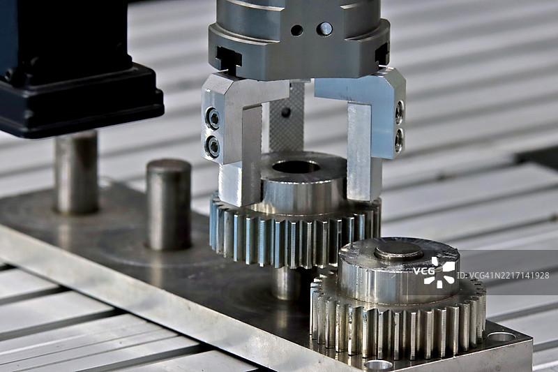 机器人手臂在自动化装配过程中抓取金属齿轮图片素材