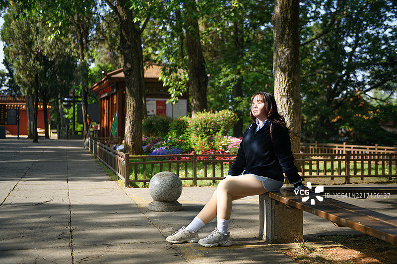 年轻女性侧身坐在公共公园的长椅上图片素材