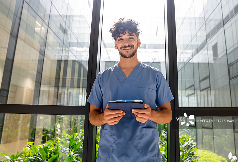 微笑着在医院里拿着平板电脑的男护士肖像图片素材