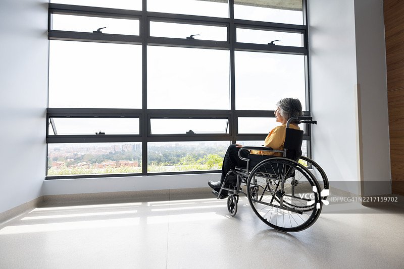 医院里坐在轮椅上的老年女性透过窗户望去图片素材