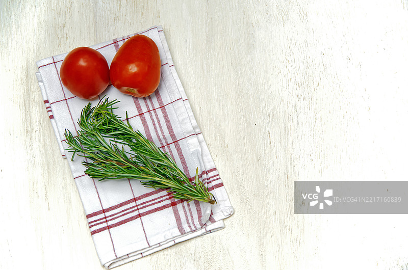 两颗红番茄和一枝迷迭香放在红白相间的餐巾上，背景为白色。图片素材