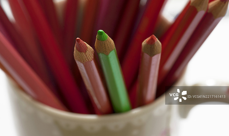 特写镜头，展示一个杯子里装着几支红色铅笔和一支绿色铅笔，采用选择性对焦。图片素材