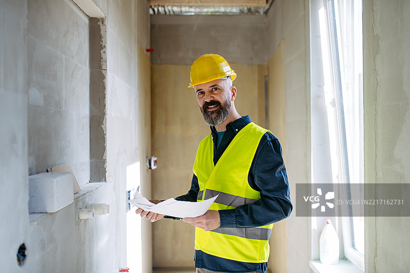 施工工程师在现场查看蓝图，头顶上方是吊顶空调。图片素材