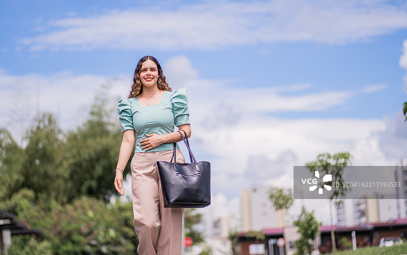 年轻女性在阳光明媚的日子里自信地走在城市中。图片素材