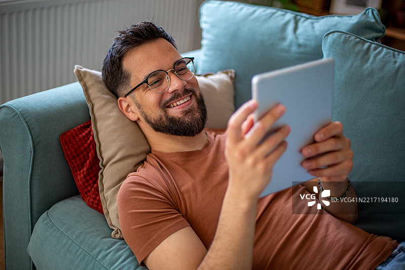 快乐的男人在家中沙发上放松，使用平板电脑图片素材