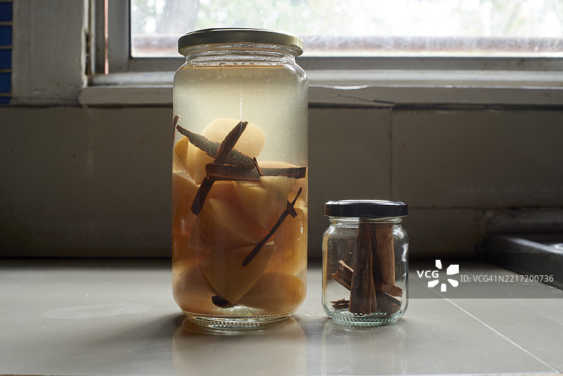 玻璃罐中展示着腌制的榅桲块和肉桂棒，静置在乡村风格的厨房台面上，突显手工食品制作技巧图片素材