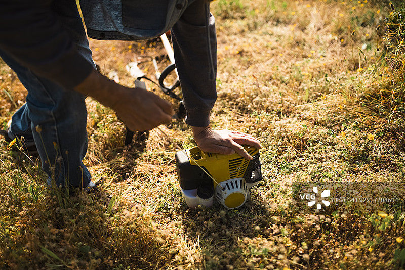 老年园丁使用汽油割草机清理和修剪草坪的手部横向视图图片素材