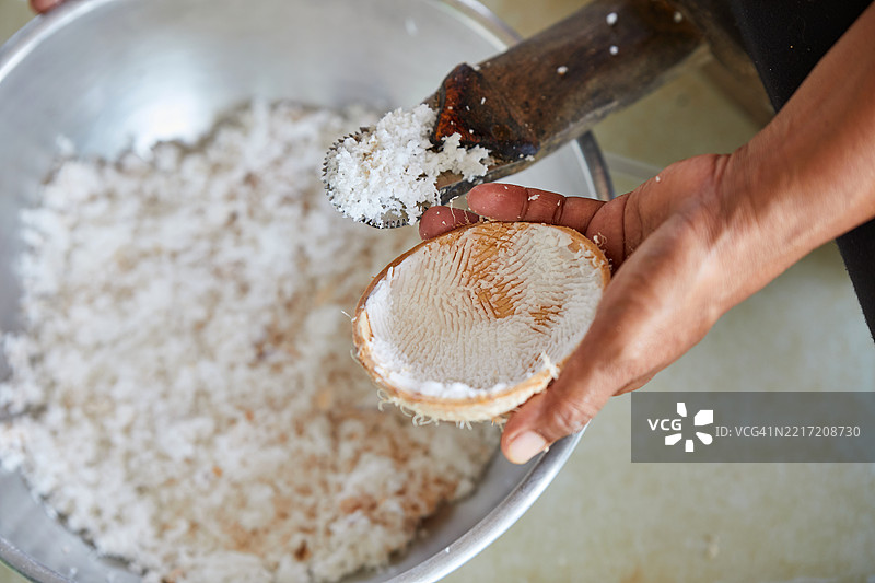 手持椰子刨刀刮削椰子壳内的白色果肉图片素材