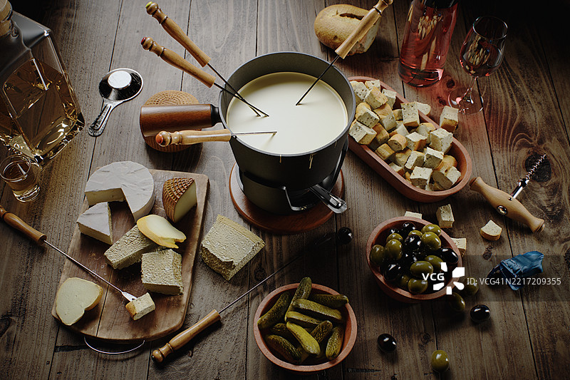 乡村风格的奶酪火锅摆盘，配有面包、橄榄和酒，放在木桌上图片素材