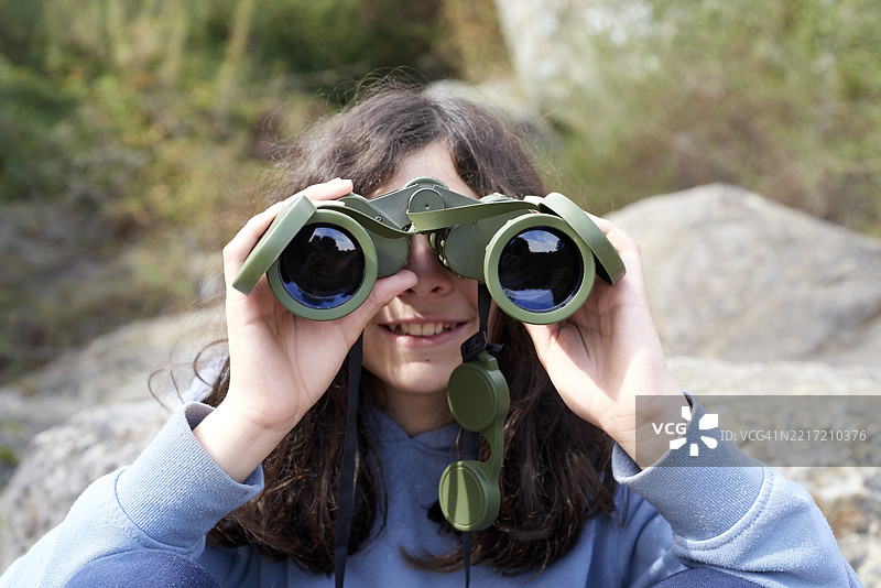 棕发少年透过望远镜微笑着，探索野外，享受户外周末冒险和自然徒步体验图片素材