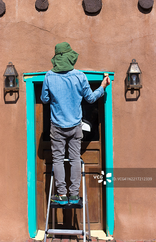 新墨西哥州圣菲：男子在涂抹青绿色门框， adobe 房屋图片素材