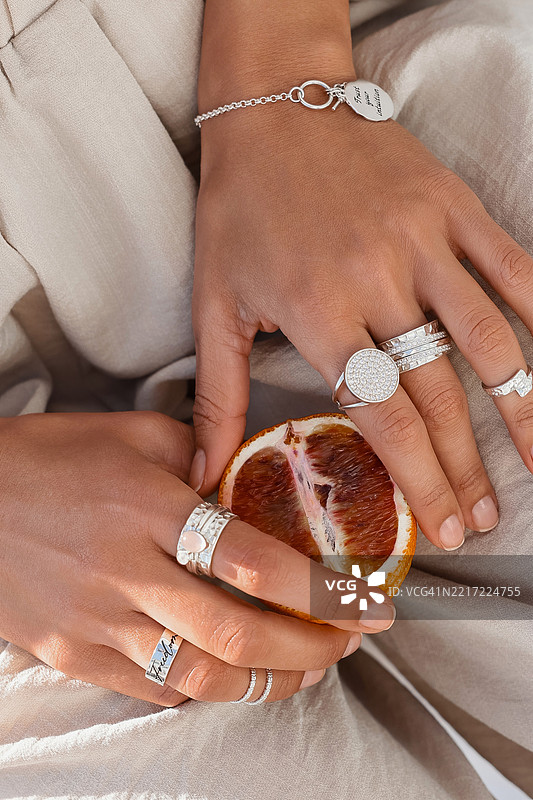 女性手上的时尚珠宝与橙子片。图片素材