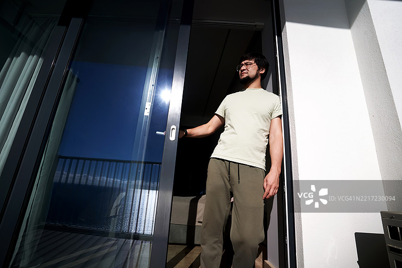 一个男人在阳光明媚的阳台门口眯着眼睛。图片素材