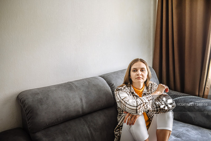 沙发上坐着一位长发女子，穿着格子衬衫，沉浸在思考中。图片素材