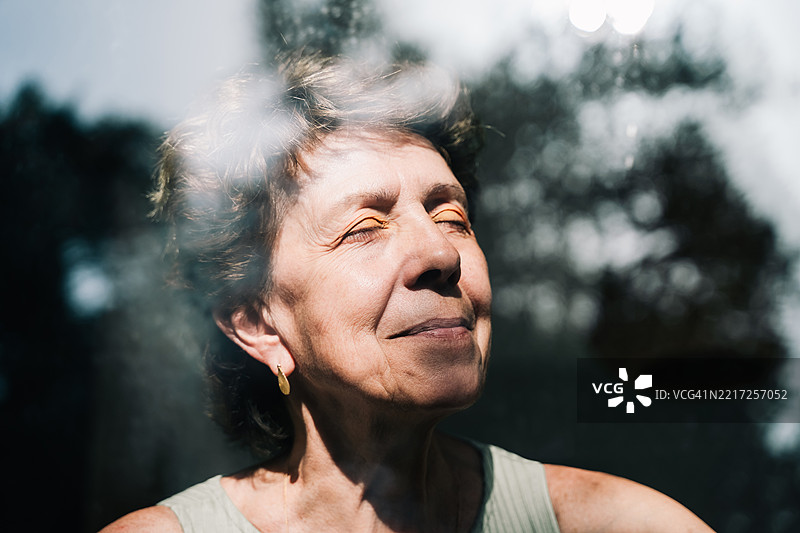 一位老年女性的特写肖像，闭着眼睛享受阳光，散发出宁静、平和和对生活的满足感。图片素材