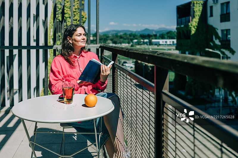 女人在阳台上阅读书籍，享受阳光明媚的日子图片素材