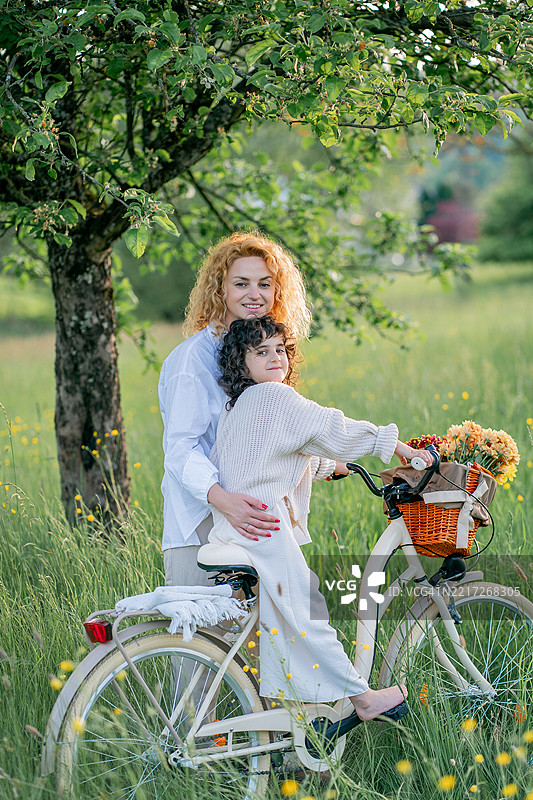 母女俩在花海中骑自行车，享受阳光明媚的一天。图片素材