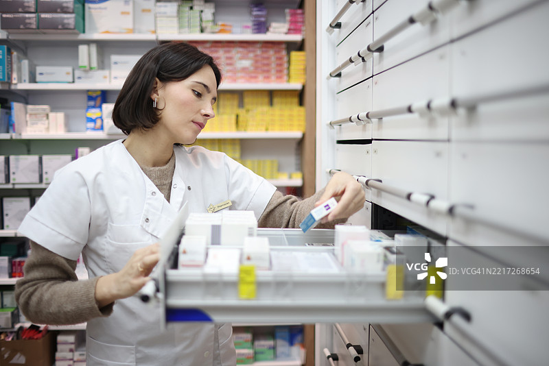 一位在药店工作的女性，将药品放入储藏室的抽屉中图片素材